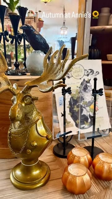 A brass stag candle holder beside terracotta votives on a warm wood counter