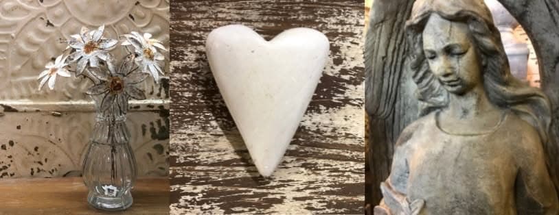 Metal daisies in a glass vase and a carved stone heart against chippy white paint